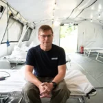 Photo of Professor Angus Watson OBE sitting on a bed in a hospital